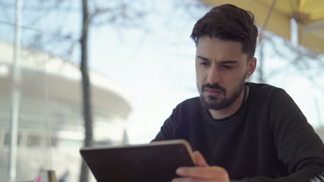 Hombre-Dudoso-Usando-Tableta-Digital-En-Un-Café-Al-Aire-Libre